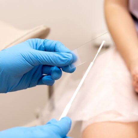 Un doctor ce poartă mănuși ține două instrumente în fața unei femei tinere