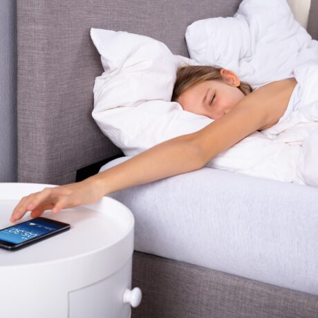 Femeie în pat care orește alarma telefonului, sugestiv pentru ce să nu faci niciodată dimineața