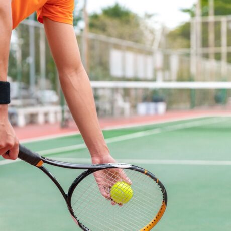 Un bărbat tânăr care ține o paletă de tenis în mână și o minge, pe un teren de tenis